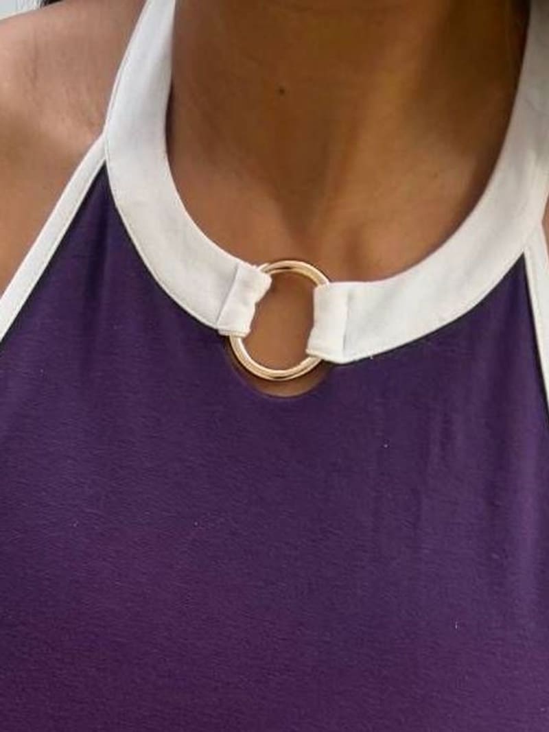 Close view of a plum halter neckline: a white collar joined at the front by a gold-tone ring, with white binding along the armholes.